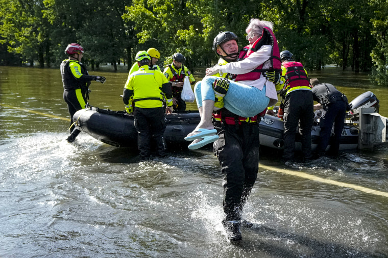 A firefighter carries a resident evacuated in a boat.