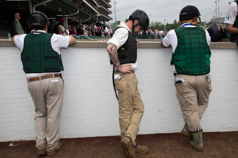 Horse riders in vests and boots wait near the track.