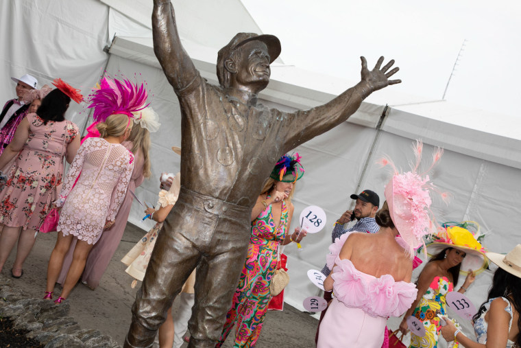 Attendees in dresses and hats near a statue of Pat Day, a jockey.