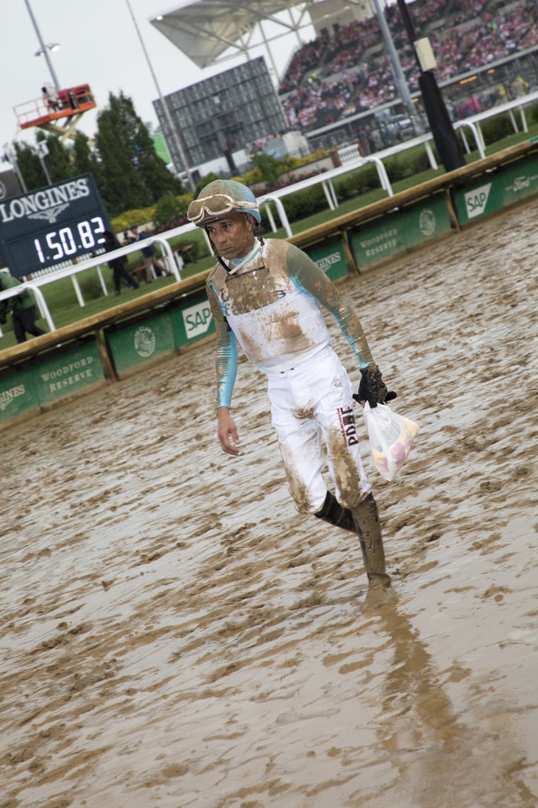 A jockey, caked in mud, walks through the muddy track at Churchill Downs.