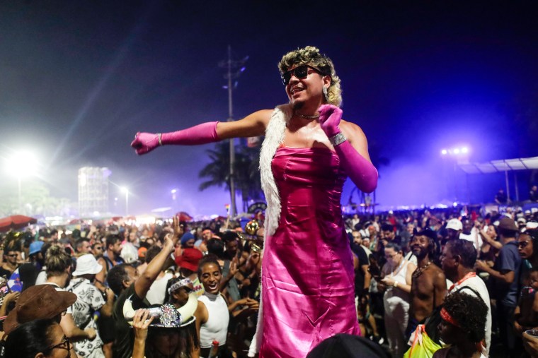 A member of the crowd dances in a pink dress, gloves, and white boa scarf