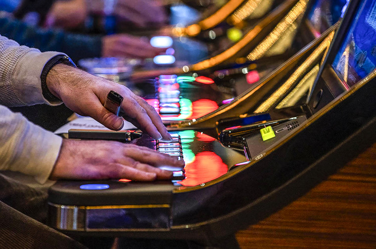 A visitor plays a slot machine with others nearby at a casino 