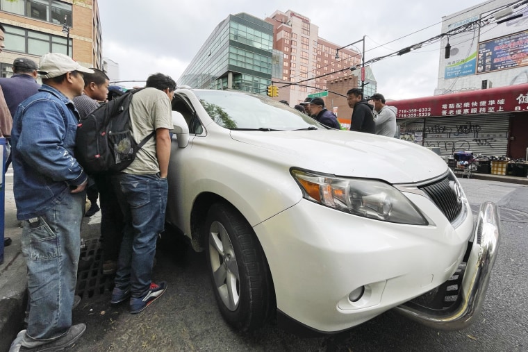 Wang Gang, 36, center left wearing backpack, talks with the driver of a car as he and others try to get a job for the day in Flushing, Queens, on May 3, 2024. 