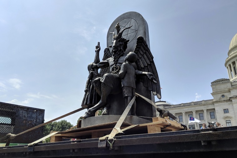 Image: A statue of Baphomet surrounded by children. Baphomet sits on a throne adorned with a pentagram.