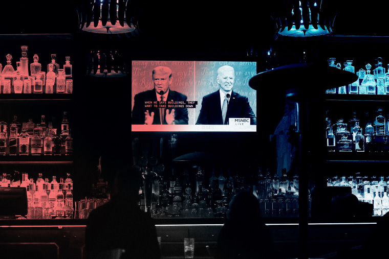 People watch a split screen of the of the  debate on a television at a bar