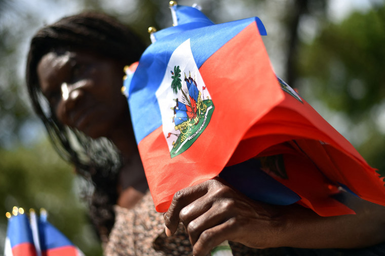A woman sells Haitian national flags while looking at a group perform a dance during the celebration of Flag Day