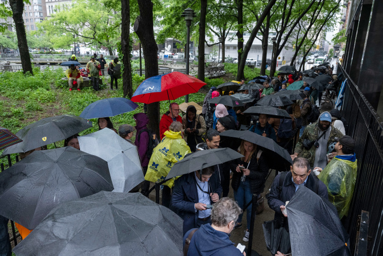 People hold umbrellas as they wait in line in the rain 