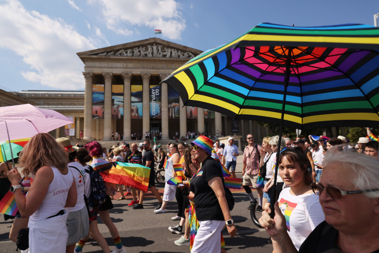 Attendees with umbrellas and rainbow flags march during Pride event. 