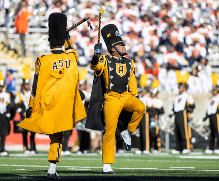 The Arizona State University marching band marches on a football field in yellow and black costumes