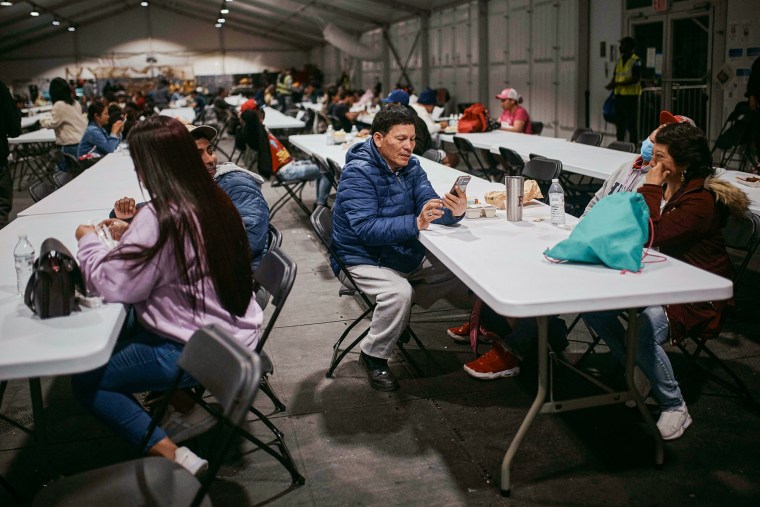 Cesar Anibal Bonilla Estrada, center, checks his phone during dinner time inside of the tent