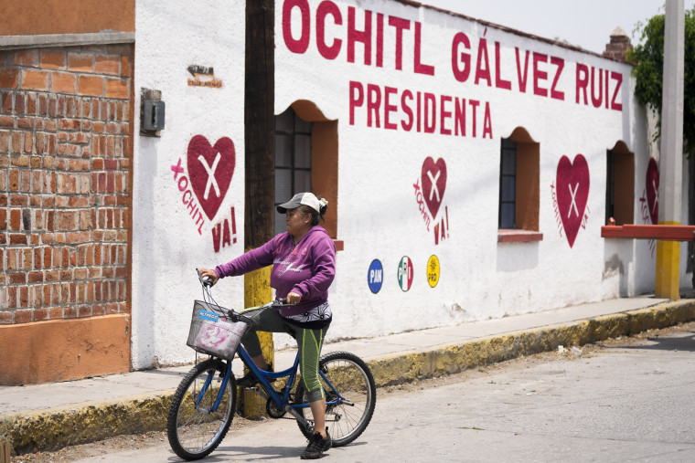 A woman rides her past a political mural promoting presidential candidate Xóchitl Galvez.