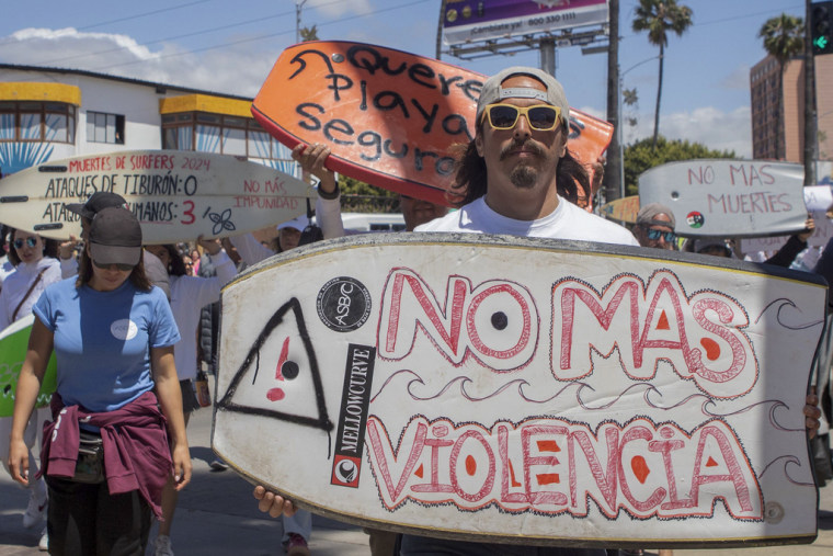 Un manifestante sostiene un tabla de surfing con el mensaje "No más violencia", en Ensenada, México, el 5 de mayo de 2024.