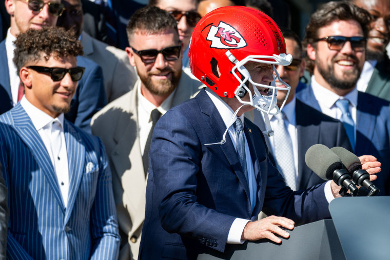 (L-R) Kansas City Chiefs' quarterback Patrick Mahomes and tight end Travis Kelce look on as US President Joe Biden wears a Chiefs helmet while speaking during a celebration for the Kansas City Chiefs.
