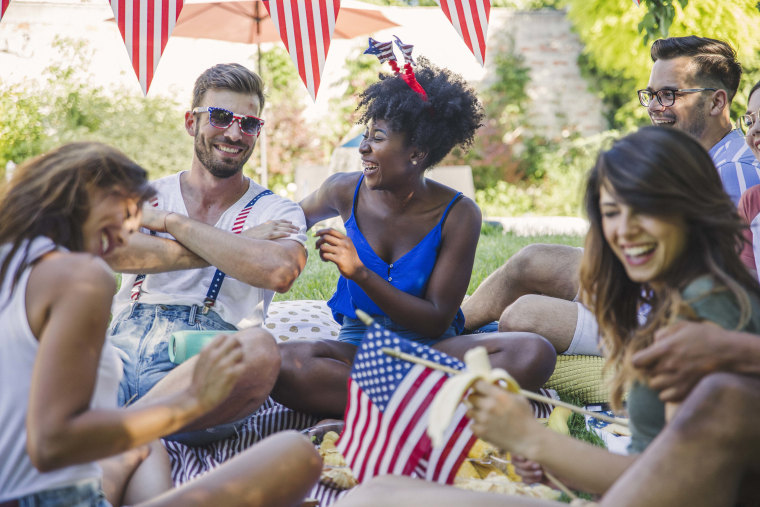 friends in backyard on picnic blanket with American flags.