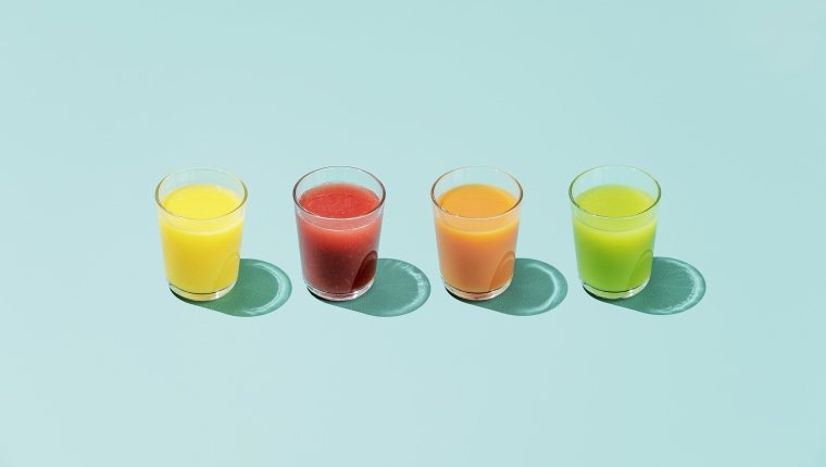Four glasses of different colored juice on a colorful background.