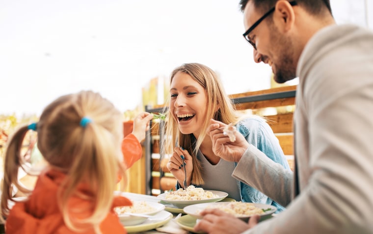Young mom and dad enjoying food at a restaurant with young daughter.