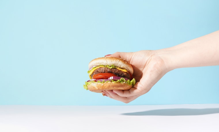 Hand holding a burger on blue background.