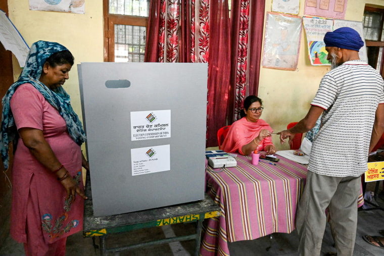 A woman casts her ballot to vote as a polling official applies indelible ink to another voter.