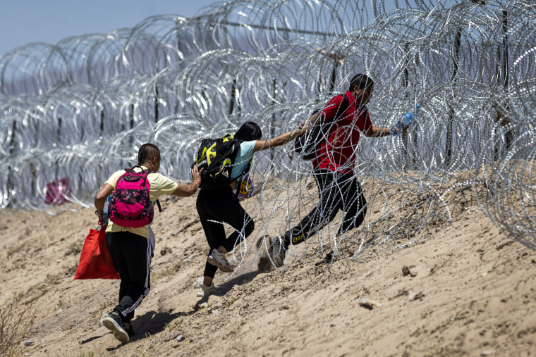 Immigrants walk through razor wire surrounding a makeshift migrant camp.