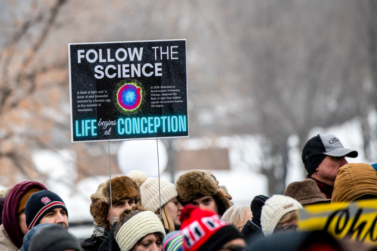 A sign at a protest reads: "Follow the Science, Life begins at Conception"