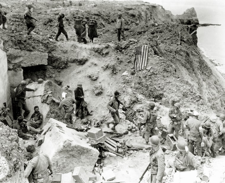 After the 2nd Ranger Battalion's attack on the Pointe du Hoc cliffs, German prisoners are rounded up and the American flag is raised for the signal in June 1944.