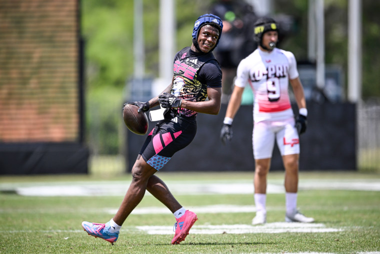 Vernell Brown III runs holding a football on the field, with Tyson Leau in the background