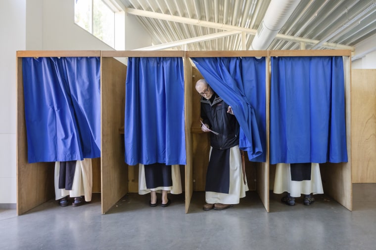 A monk opens the curtain to a voting booth in Belgium