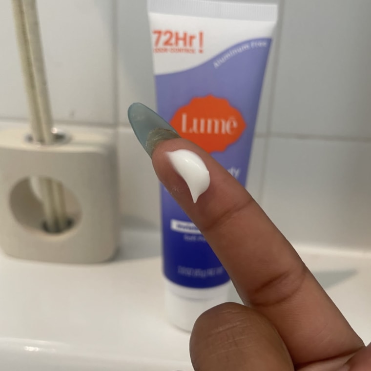 A drop of the Lume Whole Body Deodorant shown on a fingertip in front of a sink, with the deodorant tube on the counter in the background.