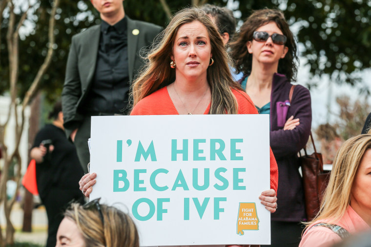 A woman holds a sign that says "I'm here because of IVF"