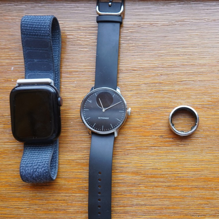 ایک Apple Watch Series 9، Withings Scanwatch Light، Oura Ring اور Apple Watch SE لکڑی کے شیلف پر۔