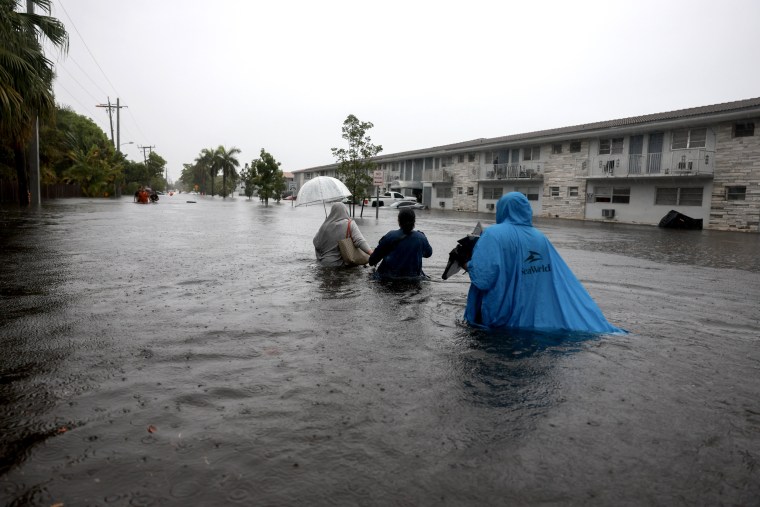 People walk through a flooded street in Hollywood, Fla.