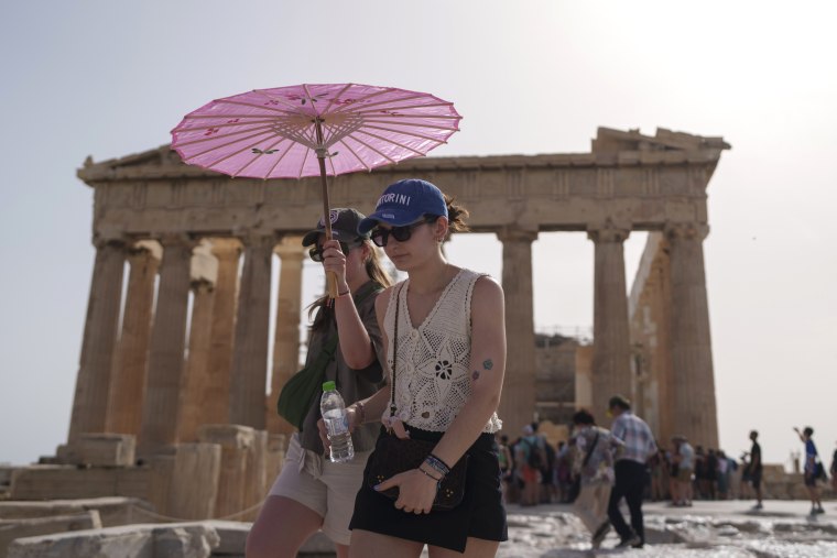Tourists with an umbrella walk in front of the Parthenon at the ancient Acropolis in Athens