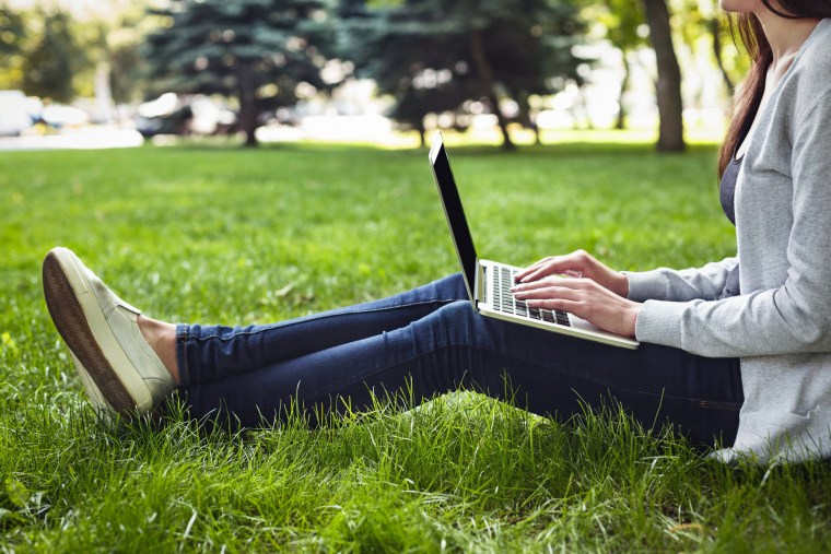 Young unrecognizable woman sitting outdoors on grass with laptop