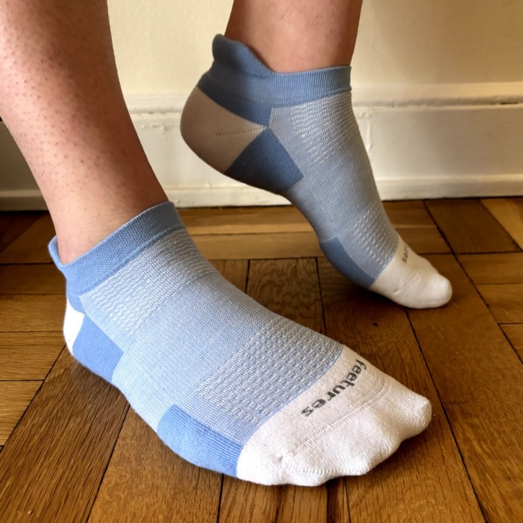 Malin wears blue socks with her back foot arched to show the design of the sock, including the tab and no-toe seam