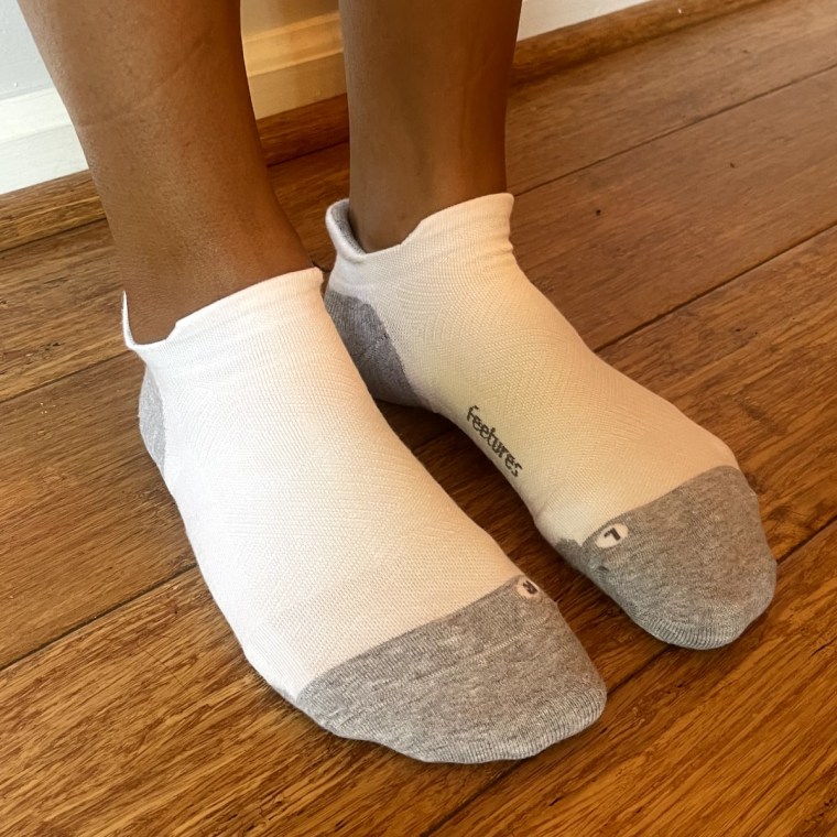 Woman wears a pair of white Feetures no-show socks on both feet without any shoes