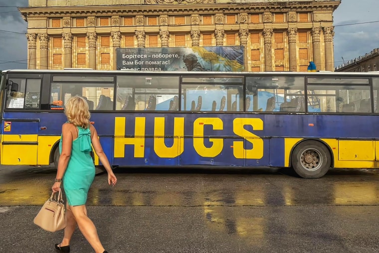 A woman passes a bus in central Kharkiv on June 12, 2024. Behind, the Kharkiv city hall displays a banner reading "Fight, you will win - God will help you!".