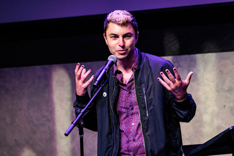 Adam Odsess-Rubin stands on stage, both hands raised as he speaks