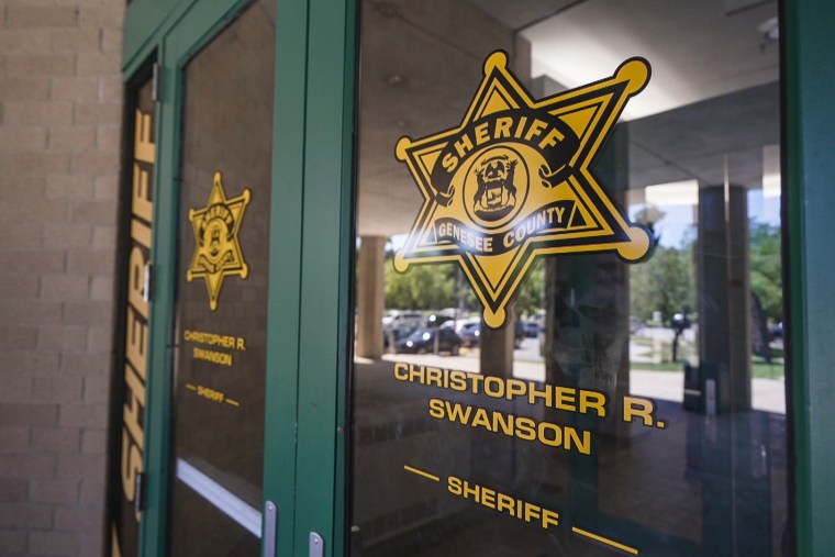 The doors of the The Genesee County Sheriff's Office, a badge and the sheriff's name, Christopher R. Swanson are on the windows