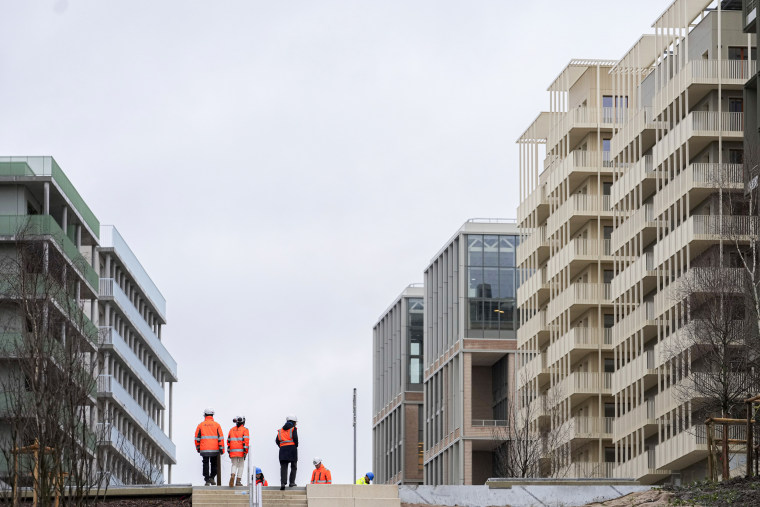 Workers stand among the buildings of the Olympic village