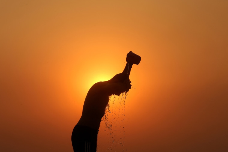 A laborer is silhouetted against the setting sun as he bathes on a hot summer day in Jammu