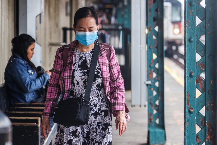 A woman with a mask walks down an outdoor subway station