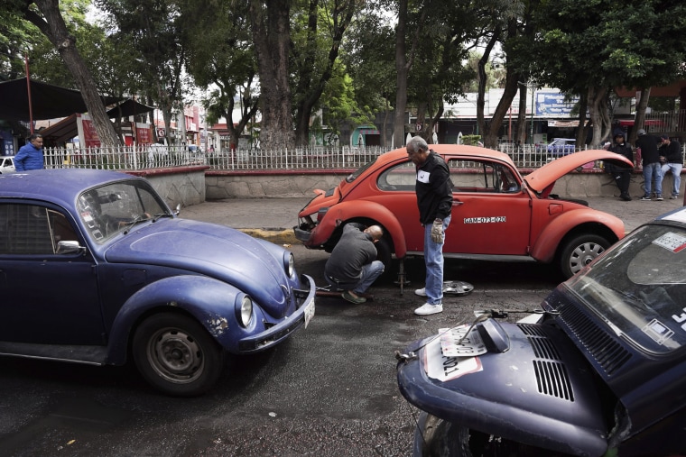 Volkswagen Beetle taxi drivers change a flat tire in Mexico City