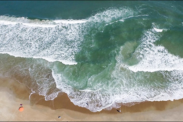 An aerial view of a wave hitting the shoreline, forming an isolated pool in the middle of the wave