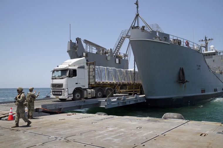 A U.S. Army soldier gestures as trucks loaded with humanitarian aid arrive at the U.S.-built floating pier Trident before reaching the beach on the coast of the Gaza Strip, Tuesday, June 25, 2024. 
