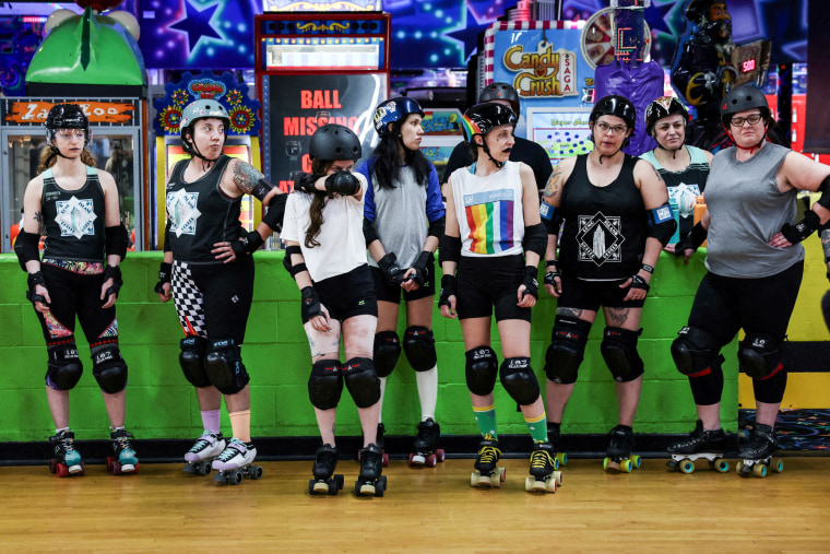 A row of roller skaters stand on the sideline of a roller skating rink