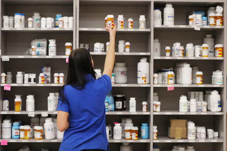 A pharmacy technician grabs a bottle of drugs off a shelf at a pharmacy
