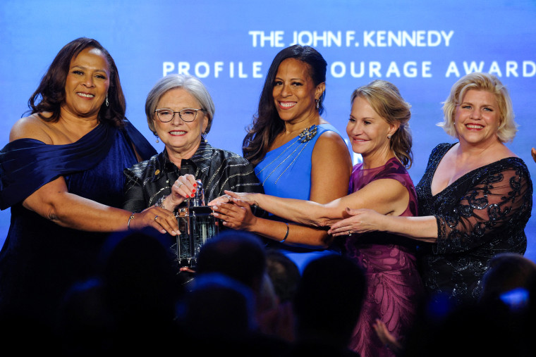 From left, Margie Bright Matthews, Katrina Shealy, Mia McLeod, Sandy Senn and Penry Gustafson all stand next to each other and place their hands on the award trophy.