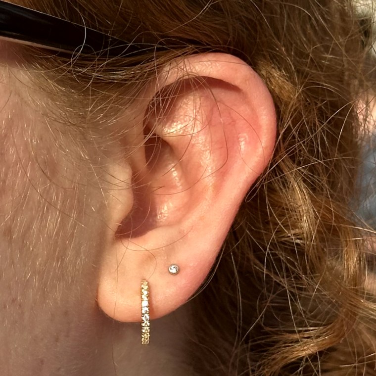 A woman pairs thin, gold, crystal-lined Rowan CZ 11mm Hypoallergenic Hoops with a simple circular second piercing.