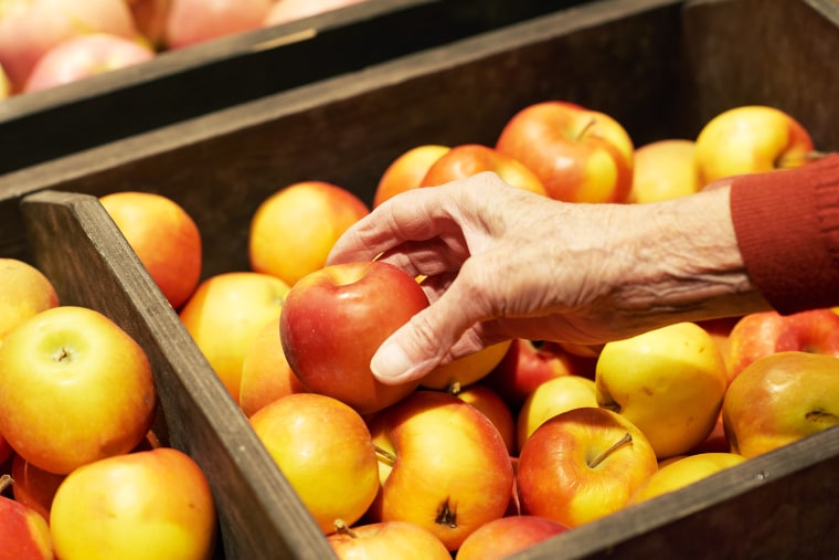 An elderly person reaches for an apple in a store