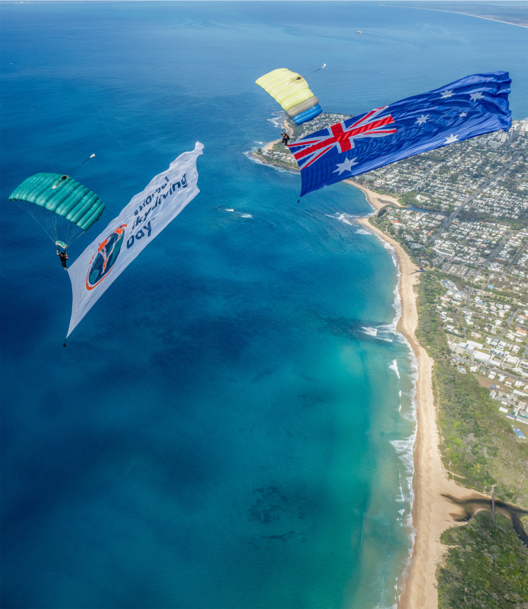 Skydivers with a flag that reads "World Skydiving Day."